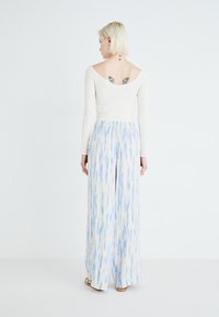 White long-sleeve top with a V-neck, paired with light blue patterned wide-leg pants featuring vertical brushstroke designs.