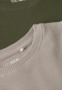 Gros plan sur des hauts à col rond en tissu côtelé, un beige superposé sur un vert olive, montrant les détails de l'encolure et la texture.