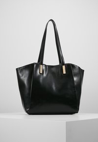 Black leather tote bag with a sleek, structured shape. Features long handles and gold-tone hardware accents. Smooth texture, no patterns.