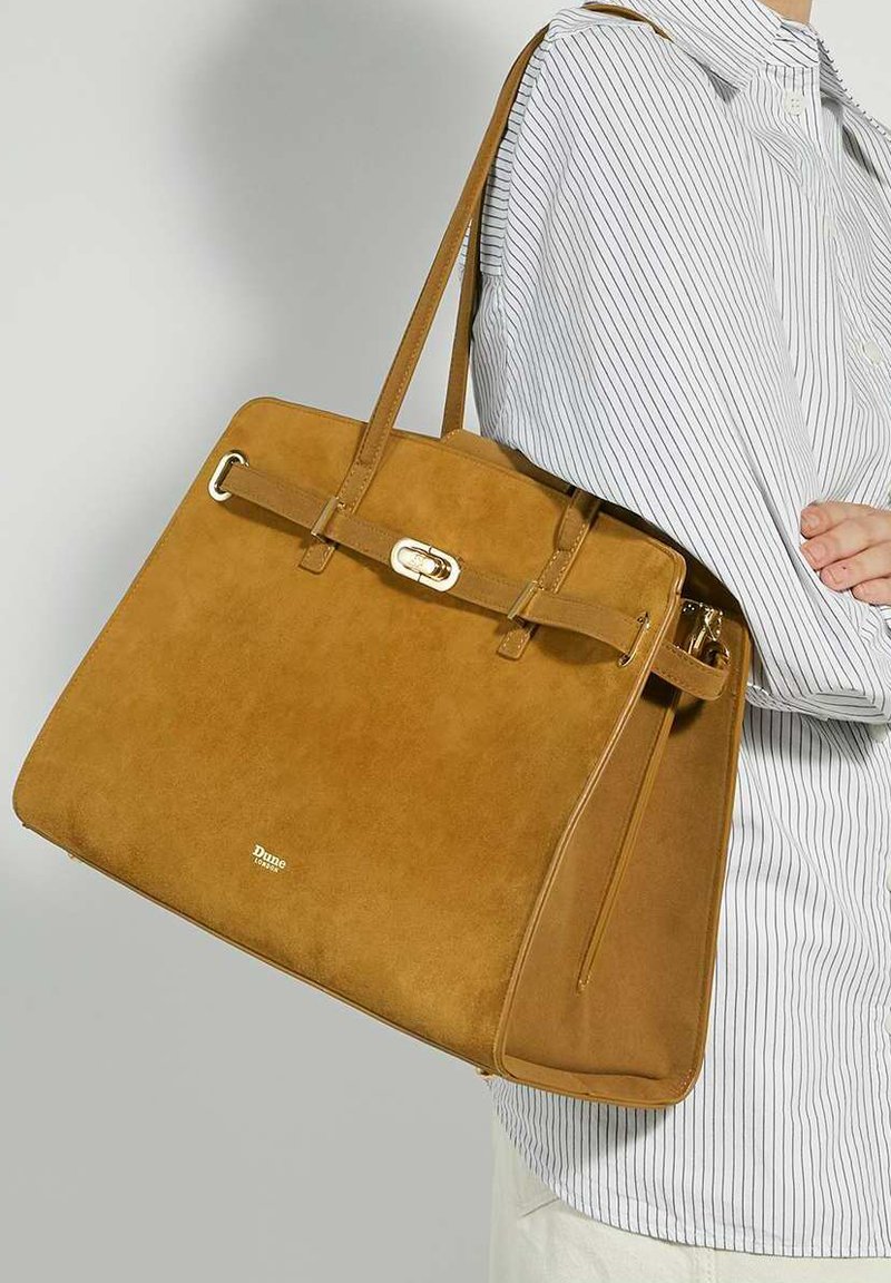 Tan suede handbag with a structured shape, featuring a front buckle closure, dual handles, and a zipper pocket on the side.