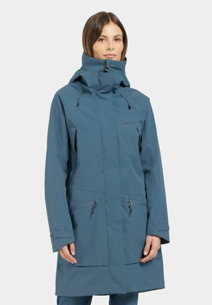 Veste imperméable bleue avec col montant, capuche ajustable, poches zippées sur la poitrine et sur les côtés, et une coupe légèrement décontractée. Texture lisse.