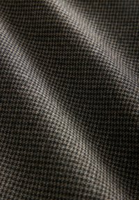 Gros plan sur un tissu à motif pied-de-poule marron et noir, avec une texture visible et des plis doux.