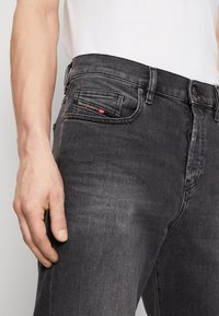 Mörkgrå denimjeans med smal passform, med en liten framficka och röd- och svart brandingdetalj på midjan.