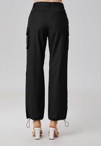 Pantalons cargo noirs avec une coupe décontractée, dotés de poches latérales, de poches arrière et d'ourlets à cordon de serrage. Texture lisse et tissu léger.