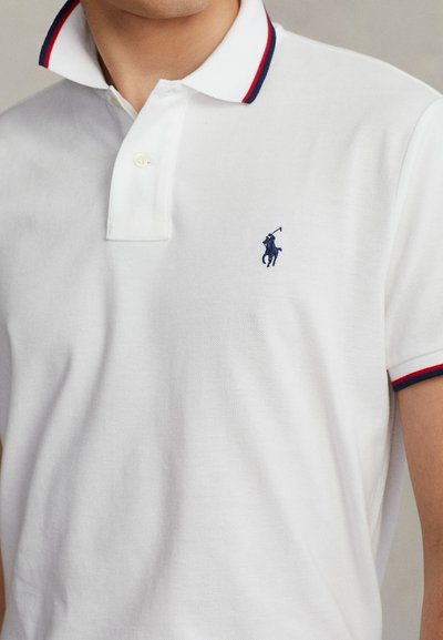 Polo branca de algodão, com abertura de dois botões, gola contrastante em vermelho e azul-marinho, e pequeno logótipo bordado no peito.
