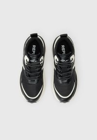 Baskets de la marque Replay en noir et blanc avec des lacets à motifs, des semelles épaisses et des languettes à l'arrière, vues de dessus sur un fond uni.