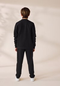 Conjunto de sudadera y pantalones de chándal negros, con un diseño clásico y puños acanalados. Zapatillas blancas que complementan el conjunto.