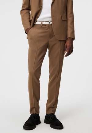 Braune, maßgeschneiderte Hose aus weichem Stoff, mit schmaler Passform und Bundfalten. Getragen mit einem weißen Gürtel und schwarzen Schuhen.
