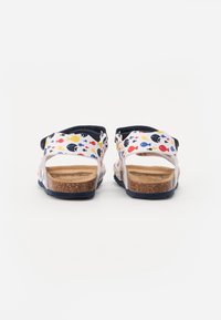 Hátulnézet a szandálról, amely fehér alapon színes halmintázattal, parafa talppal, tengerészkék akcentussal és nyitott sarokkal rendelkezik a légáteresztő képesség érdekében.