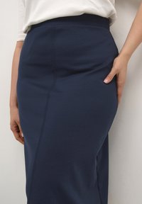 Jupe ajustée bleu marine en matériau doux, avec une texture lisse et une couture sur le devant, stylisée avec une taille haute.
