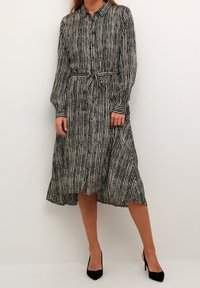 Schwarz-weißer gestreifter Hemdkleid mit langen Ärmeln und Bindegürtel. Midi-Länge mit leicht ausgestellt geschnittenem Saum und spitzem Kragen.