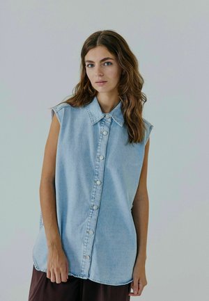 Camicia senza maniche in denim azzurro chiaro con bottone frontale, colletto a punta e vestibilità rilassata. Tessuto liscio, orlo arrotondato e accenti minimi.