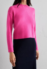 Różowy dziergany sweter z długimi rękawami i okrągłym dekoltem, zestawiony z granatową prążkowaną spódnicą z subtelnymi wzorami.