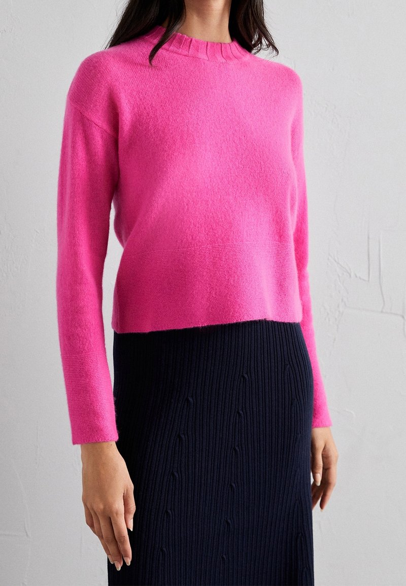 Różowy dziergany sweter z długimi rękawami i okrągłym dekoltem, zestawiony z granatową prążkowaną spódnicą z subtelnymi wzorami.