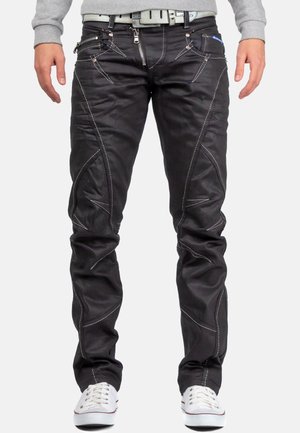 Zwarte denim broek met zilveren stiksel, voorzien van meerdere met rits afgesloten zakken en een asymmetrisch nadenontwerp. G gedragen met een lichtgrijze sweatshirt.