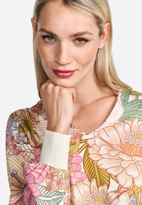 Floral long-sleeve top featuring a v-neckline. Soft fabric with a colorful floral pattern in pink, yellow, and green. Ribbed cuffs.