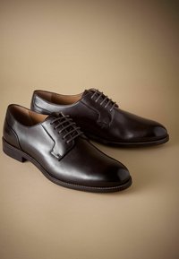 Zapatos de vestir de cuero marrón con un acabado suave. Con un diseño de cordones, punta redondeada y detalles cosidos a lo largo de la suela.