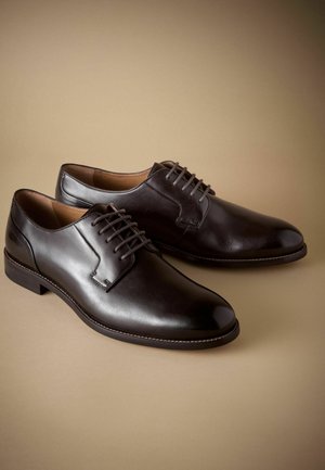 Zapatos de vestir de cuero marrón con un acabado suave. Con un diseño de cordones, punta redondeada y detalles cosidos a lo largo de la suela.