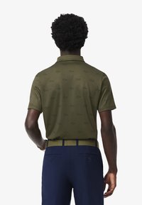 Camisa polo verde oliva con un patrón sutil, de manga corta y con cuello. Combinada con pantalones azul marino y un cinturón verde oliva.