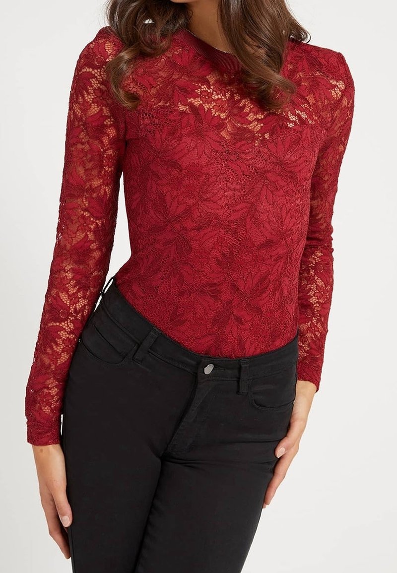Bodysuit rouge en dentelle à manches longues avec des motifs floraux et une coupe ajustée, associé à un jean noir. Texture lisse et col rond.