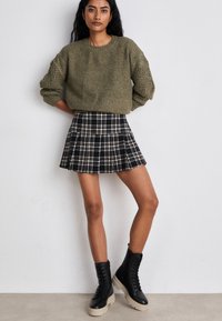 Khaki sweter dziany z teksturowanymi, luźnymi rękawami, zestawiony z czarną i białą spódnicą w kratę z plisami oraz masywnymi czarnymi butami na sznurówki.