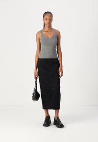 Hallika ribiline tank top on kombineeritud musta nööpidega midi seelikuga. Mudel hoiab väikest musta käekotti ja kannab paksu musta jalatsit.