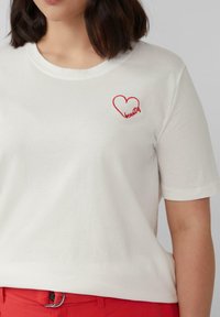 Weißes Baumwoll-T-Shirt mit kurzen Ärmeln, rundem Ausschnitt, versehen mit einem roten gestickten Herzen und dem Wort "Schönheit" in Rot darunter.