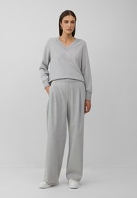 Haut tricoté texturé gris avec décolleté en V et poignets ajustés, associé à un pantalon large gris. Le mannequin porte des baskets blanches. Design simple et élégant.
