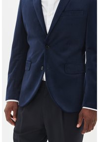 Navyblaues Samtblazer mit Revers, Ein-Knopf-Verschluss und zwei Vorderpockets. Sanfte Textur mit taillierter Passform.