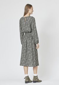 Langærmet kjole i sort og hvid leopardprint, med en nøglehul detalje i ryggen, snøret talje og svajende skørt. Bæret med grønne ankelstøvler.