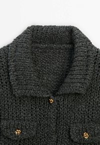 Cardigan grigio lavorato a maglia con ampio colletto, bottoni in tono dorato e due tasche frontali. La texture è spessa e robusta.