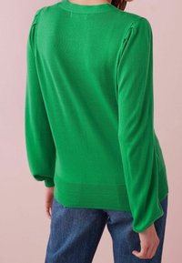 Pullover verde lavorato a maglia con maniche lunghe e leggermente arricciate, fondo a coste e texture liscia, abbinato a jeans in denim blu.