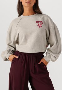 Grijze sweatshirt met raglanmouwen en een bloemgrafiek, gecombineerd met bordeaux elastische broek met zijzakken.