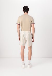 Beige t-shirt with red and blue striped cuffs, paired with light-colored striped shorts. White sneakers and crew-length socks complete the look.