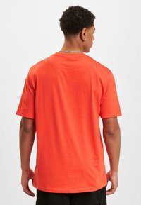 Herren T-Shirt mit kurzen Ärmeln aus leuchtend orangefarbenem Baumwollstoff, mit Rundhalsausschnitt und lockerer Passform. Glatte Textur, ohne erkennbare Muster.