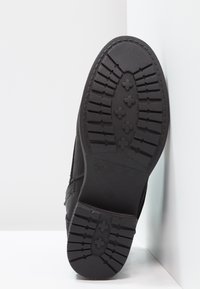 Černá podrážka boty s texturovanými vzory, obsahující žebrované a křížové tvary pro lepší přilnavost. Materiál vypadá jako guma s plochým designem.