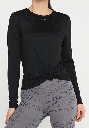 T-shirt de sport noir à manches longues avec un col rond, présentant un détail noué à la taille et un logo Nike discret sur la poitrine.