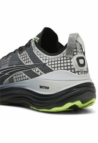 Scarpa atletica in bianco e nero con tomaia in rete, motivo a griglia e dettagli verdi. Presenta una suola spessa a forma di onda con il marchio "NITRO".