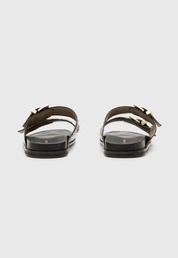 Mustad mustad, millel on kaks rihma kuldse tooniga detailidega ja lame tall. Sile viimistlus dekoratiivsete aktsentidega külgedel.