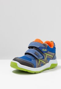 Zapatillas para niños en azul, gris y negro con un forro interior naranja, dos correas de Velcro, acentos verdes y una suela blanca con fondo verde.
