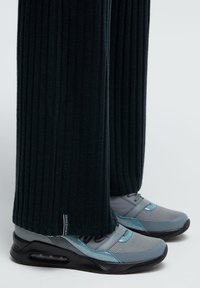 Schwarze gerippte Hose, die über graue Sportschuhe mit blauen Akzenten fällt; die Schuhe bestehen aus Mesh und festen Materialien und haben eine abgerundete Zehenpartie.