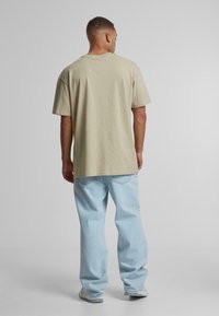 Beige cotton T-shirt with a relaxed fit, short sleeves, and a crew neckline, paired with light blue, loose-fitting jeans.