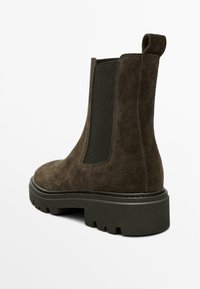 Brązowy zamszowy botek do kostki z elastycznymi panelami bocznymi, wytrzymałą podeszwą i uchwytem. Posiada okrągły czubek i teksturowane wykończenie.