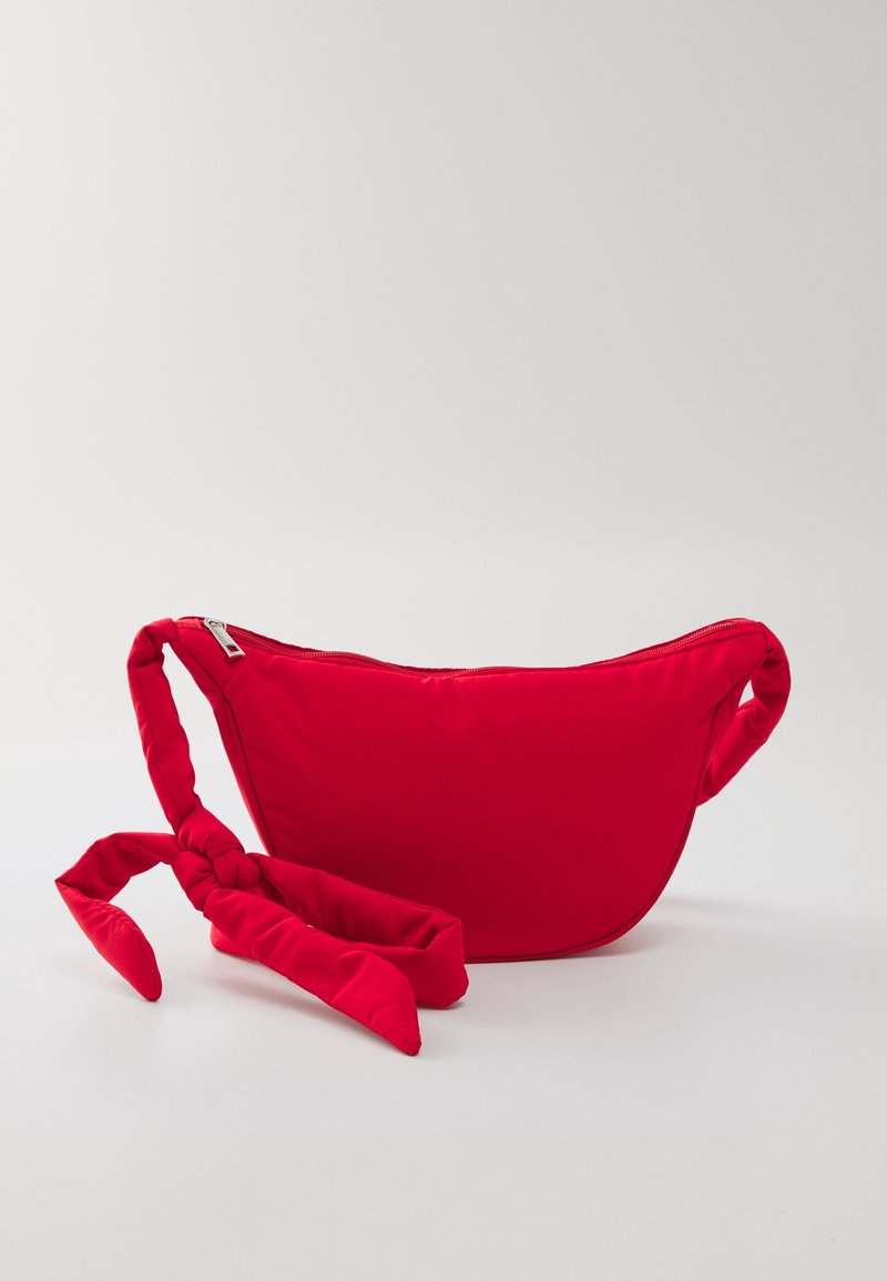 Borsa a spalla rossa in nylon con forma curva, chiusura con zip e tracolla annodata per trasporto regolabile. Texture liscia senza motivi.