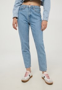 Jeans azzurri a vita alta con gamba dritta, texture in denim e cinque tasche. Abbinati a sneaker bianche con lacci rosa.