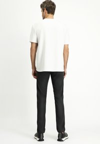 Witte T-shirt met korte mouwen en ronde hals, gecombineerd met zwarte slim-fit broek en zwarte sportschoenen. Eenvoudig, strak ontwerp.