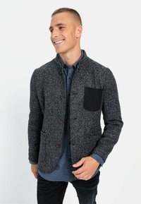 Knoopjasje van donkergrijze tweed met een gemêleerde afwerking, voorzien van een contrasterende zwarte zak en een mandarinnekraag.
