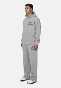 Jasnoszara bluza z kangurzą kieszenią, dopasowane spodnie dresowe oraz napis "Good for Nothing". Miękka tkanina; luźny, wygodny krój.
