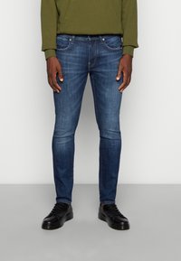 Slim-fit blå jeans i denimtyg med midjehöjd, femficksdesign, lätt bleknad yta, kombinerade med svarta sneakers.