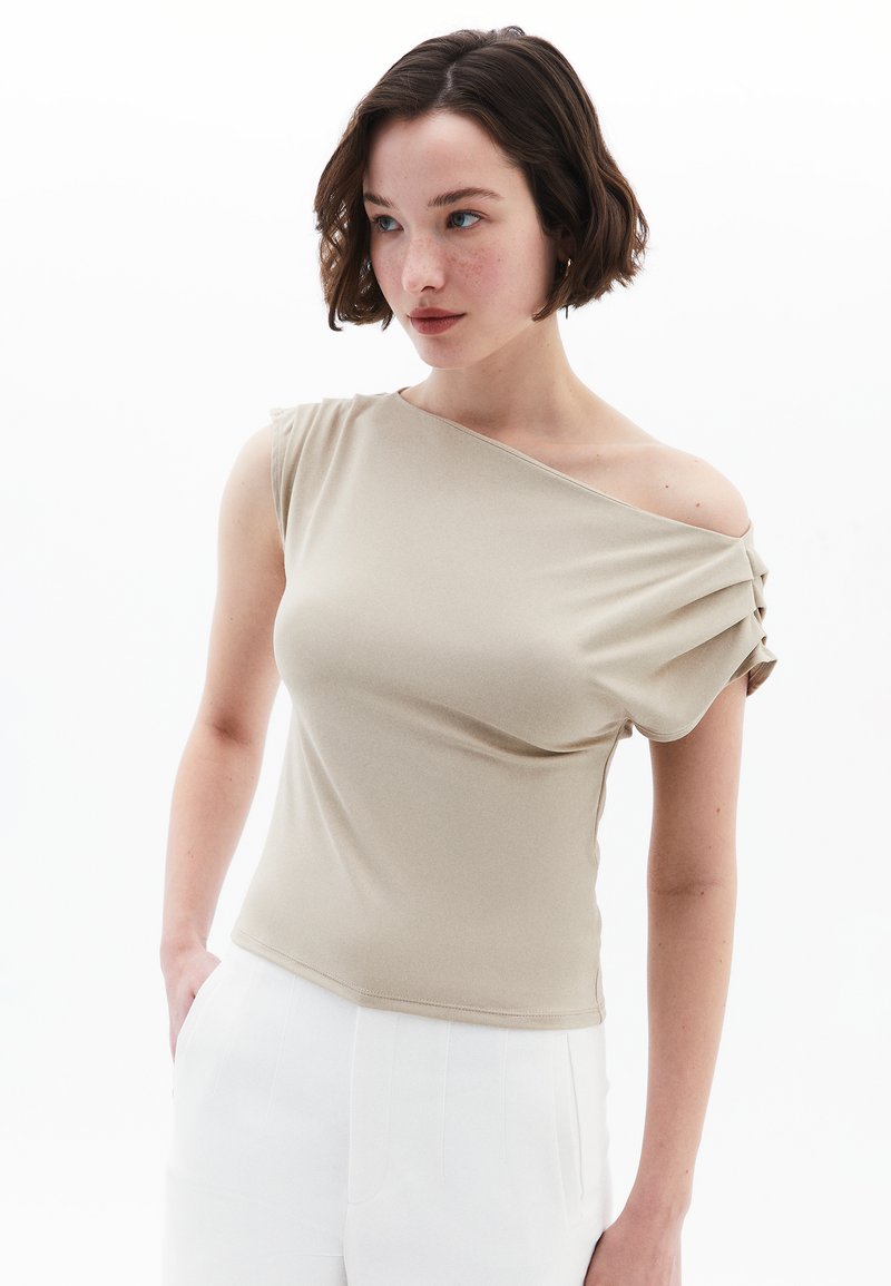 Beige, tætsiddende bluse med en off-shoulder design, korte ærmer og plisserede detaljer på skulderen. Glat stofkvalitet.